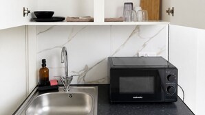 A kitchen with a black microwave, a sink, and a countertop with a coffee maker and jars. - KW SELF CONTAIN STUDIOS ALEXANDRA PALACE (London)