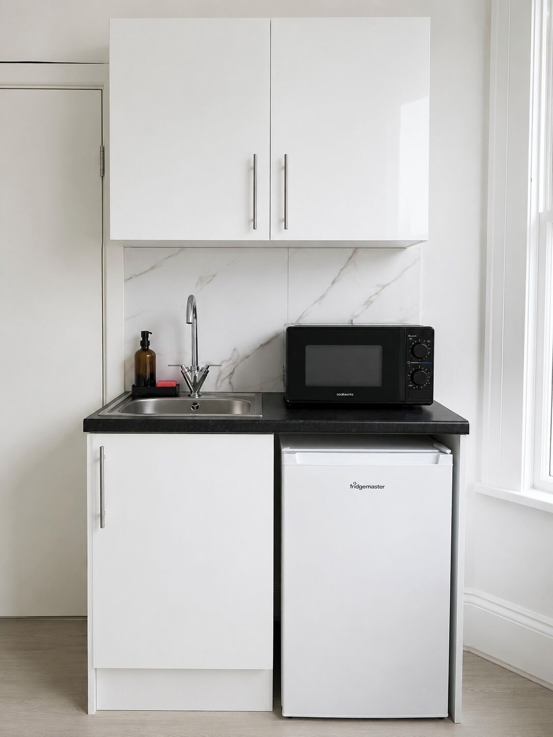 A compact kitchen with white cabinets, a black countertop, a built-in microwave, a small refrigerator, and a sink with a faucet.
