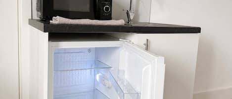 A compact kitchen with a built-in microwave, a sink, and a refrigerator with transparent drawers.