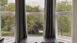 A corner room with a bay window, two chairs, and a table. - KW SELF CONTAIN STUDIOS ALEXANDRA PALACE (London)