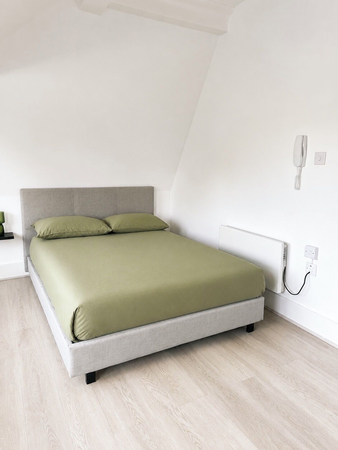 A modern bedroom with a bed, a bedside table, and a wall-mounted telephone.