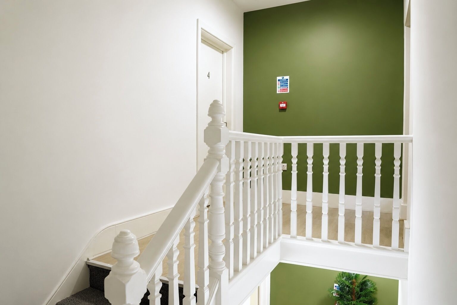 Eine Treppe mit weißen Balustraden, einer grünen Wand und einer Tür mit der Aufschrift '4'.