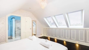 Et soveværelse med stor seng, ovenlys, walk-in closet og bruseområde.