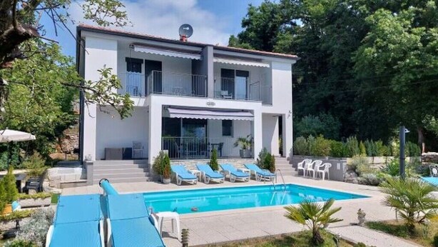 Ein zweistöckiges Haus mit Swimmingpool, Sitzgelegenheiten im Freien und einem Garten.