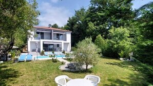 Ein zweistöckiges Haus mit Swimmingpool, umgeben von einer gepflegten Rasenfläche und Bäumen.