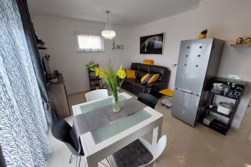 A modern living room with a dining table, sofa, and a refrigerator.