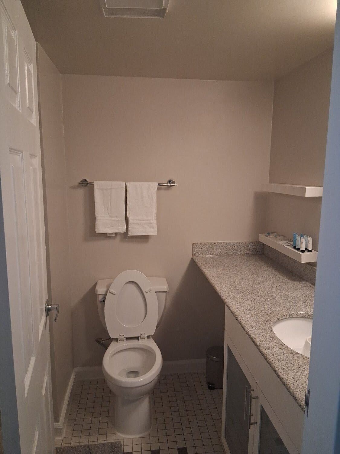 A small bathroom with a toilet, a sink, and a mirror. There are two towels hanging on a rack above the toilet.
