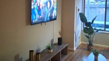 A living room with a flat-screen TV mounted on the wall, a wooden bench with potted plants, and a small table.