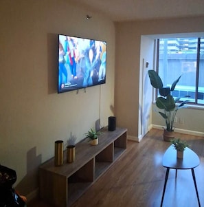 A living room with a flat-screen TV mounted on the wall, a wooden bench with potted plants, and a small table. - Prime location | Steps from Pentagon City Metro (Arlington)