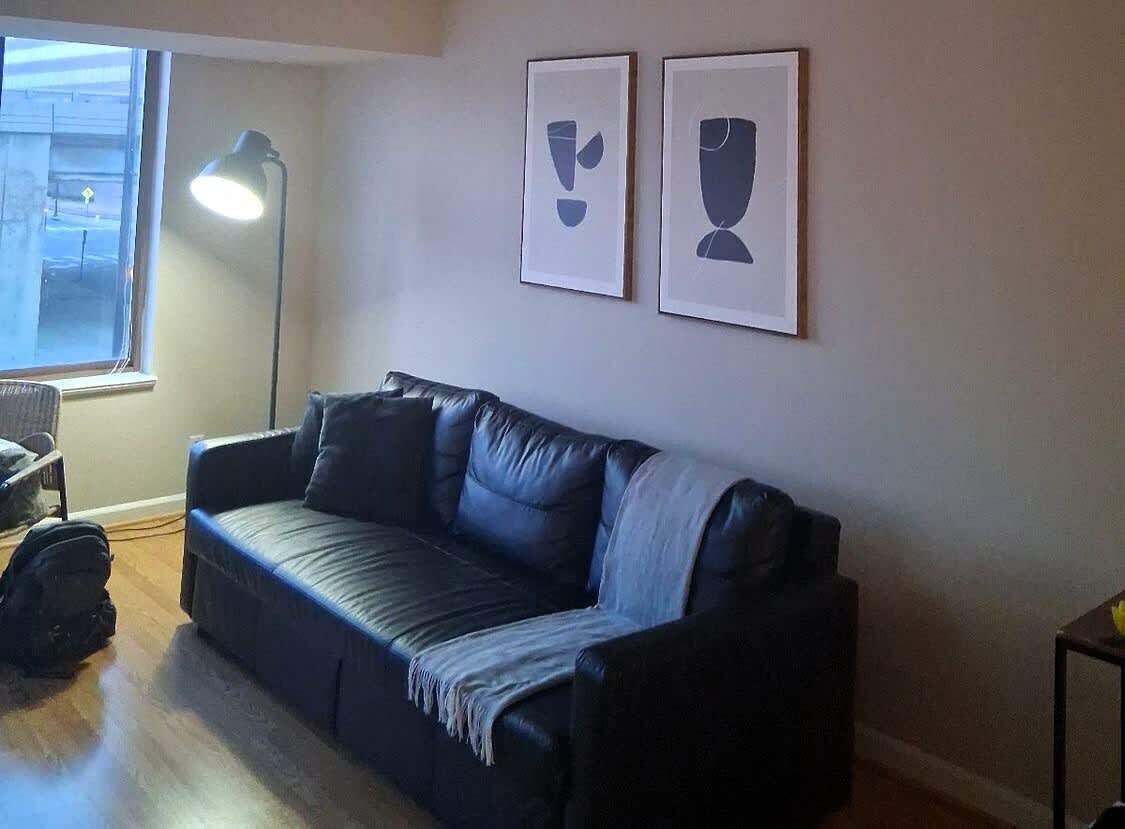 A living room with a black leather sofa, a standing lamp, and two framed abstract art pieces on the wall.