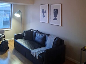 A living room with a black leather sofa, a standing lamp, and two framed abstract art pieces on the wall. - Prime location | Steps from Pentagon City Metro (Arlington)