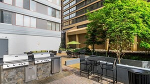 An outdoor patio with a barbecue grill, seating area, and a view of a building with large windows. - Apartment Steps from Pentagon City Metro (Arlington)