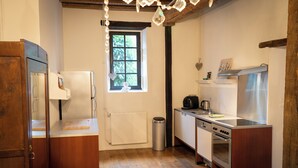 A kitchen with wooden flooring, a refrigerator, a stove, a sink, and a window with a view of greenery. - Maison 2 du domaine d'embourg (Souvigny)