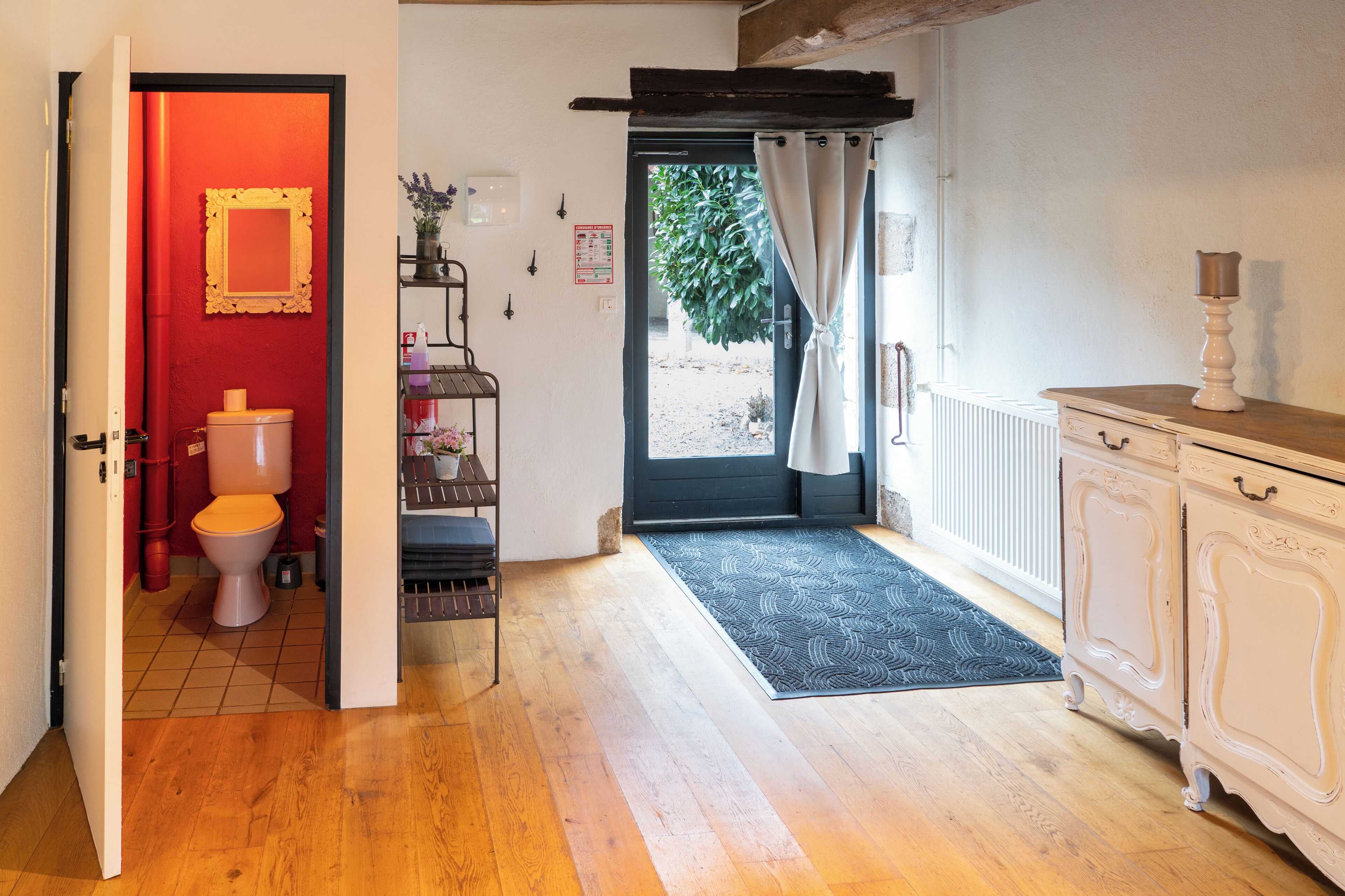 A room with a wooden floor, a white cabinet, a red door, and a view of the outside.