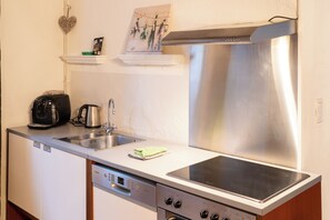 A compact kitchen with a stainless steel range hood, a built-in dishwasher, and a coffee maker. - Maison 2 du domaine d'embourg (Souvigny)