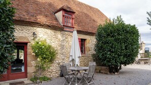 A stone building with a red door and a gravel patio with a table and chairs. - Maison 2 du domaine d'embourg (Souvigny)