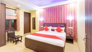 A hotel room with a large bed, a ceiling fan, a wooden bench, and a patterned wall. - Hotel O Red Stone (New Delhi)