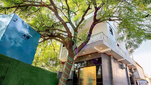 A building with a modern design, featuring a large tree wrapped with colorful lights, a visible entrance, and a sign that reads "WELCOME". - Hotel O Red Stone (New Delhi)