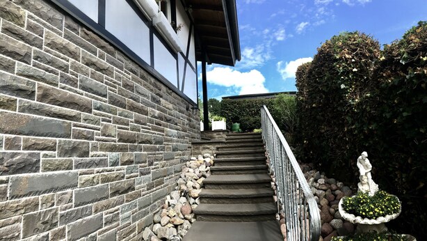 A stone staircase leading to a building with a metal railing and a statue at the bottom. - Apartment in Traditional Timber-Framed House with Garden in the Bergisches Land (Overath)