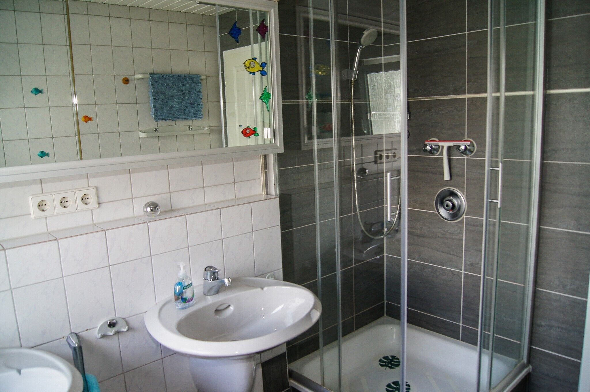 A bathroom with a white sink, a mirror, a shower with a glass door, and a tiled wall.