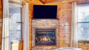 Ein gemütliches Blockhaus-Interieur mit Kamin aus Naturstein, Holzwänden und einem Tisch mit Büchern.