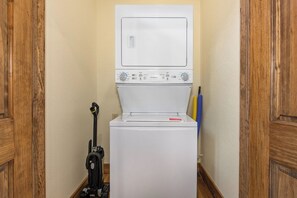 A compact, white laundry machine in a narrow hallway with wooden doors and a vacuum cleaner to its left. - Relaxing 5BD POOL Lodge| Theater + Hot Tub + Games (Sevierville)