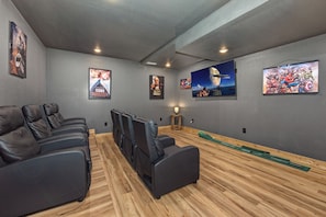 A home theater room with dark leather recliners, a wooden floor, and movie posters on the walls. - Relaxing 5BD POOL Lodge| Theater + Hot Tub + Games (Sevierville)