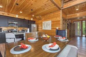 Un intérieur en bois avec une table à manger pour quatre personnes, une cuisine équipée d’appareils modernes et une grande carte du monde accrochée au mur.