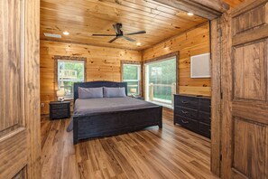A bedroom with a bed, wooden walls, a ceiling fan, and a window with blinds. - Relaxing 5BD POOL Lodge| Theater + Hot Tub + Games (Sevierville)