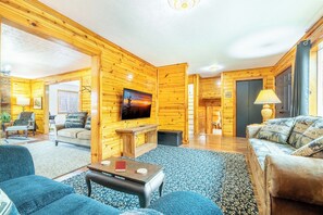 A cozy log cabin interior with a living room, a television, and a fireplace. - Beautiful 3BD Home Near TOWN | Hot Tub + Fire Pit! (Sevierville)