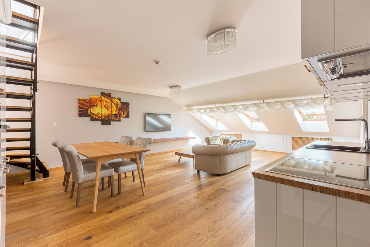 A modern apartment with a dining area, sofa, kitchen, and a staircase.
