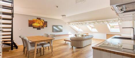 A modern apartment with a dining area, sofa, kitchen, and a staircase.