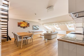 A modern apartment with a dining area, sofa, kitchen, and a staircase.