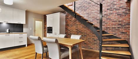 Una cocina moderna con armarios blancos, una mesa de comedor con sillas y una pared de ladrillo con una escalera de madera.