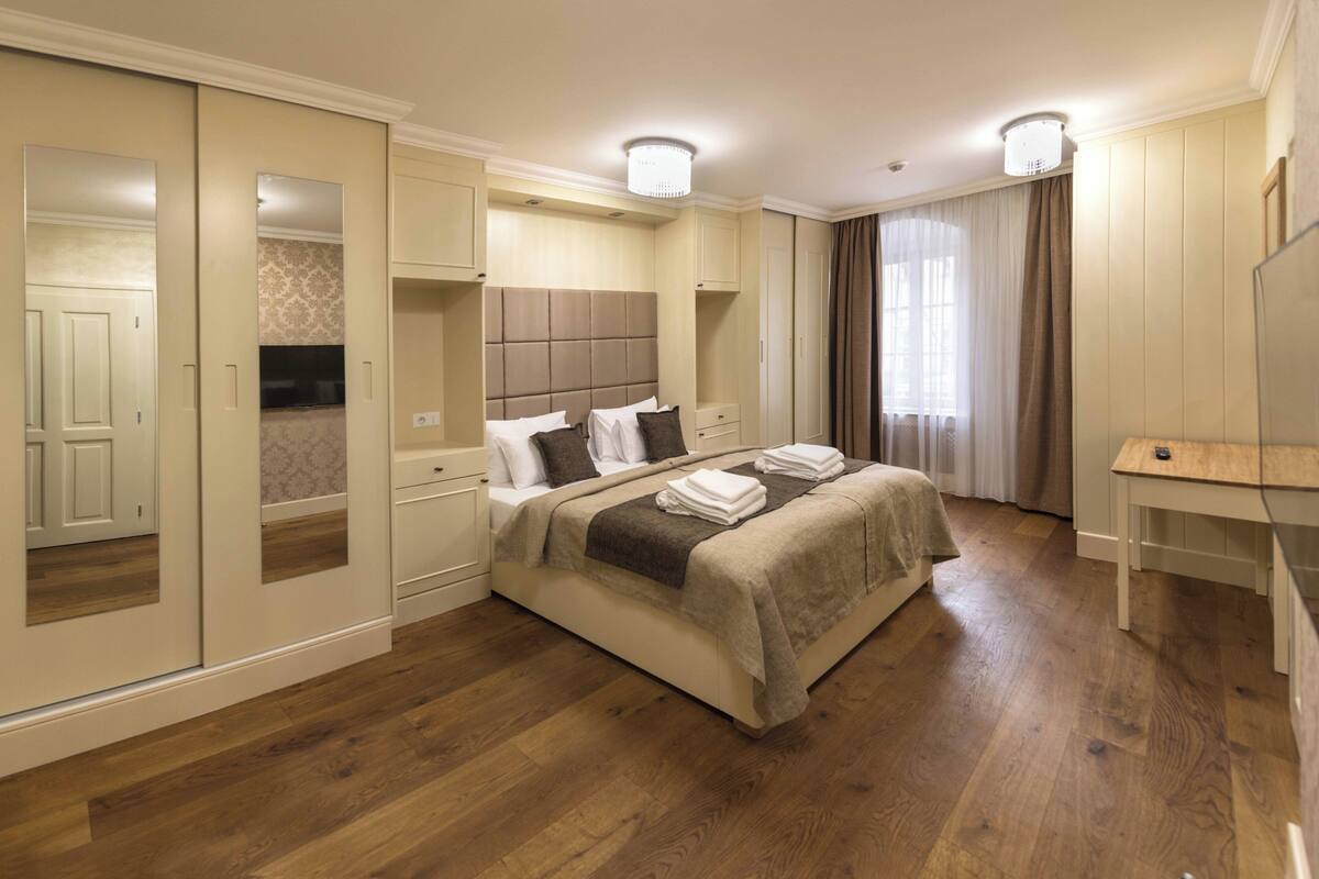 A hotel room with a large bed, a desk, a wardrobe, and a mirror.