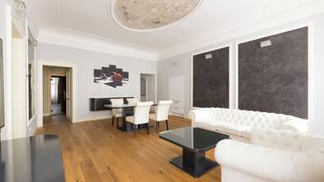 A modern living room with a white sofa, a black coffee table, and a dining area with a white table and chairs.