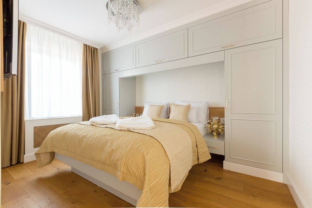 A bedroom with a bed, a bedside table, a nightstand, a wardrobe, and a chandelier.