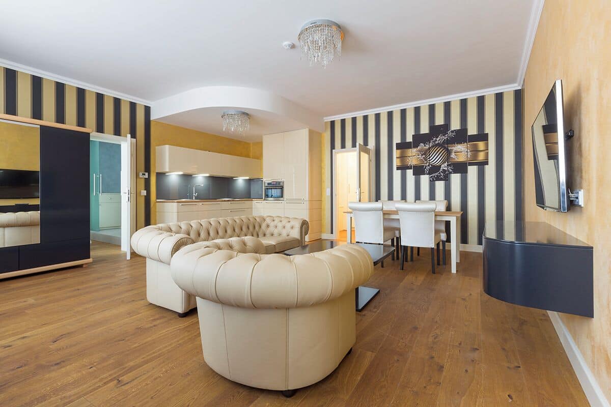 A modern living room with a curved sofa, a dining area with a table and chairs, and a kitchen in the background.