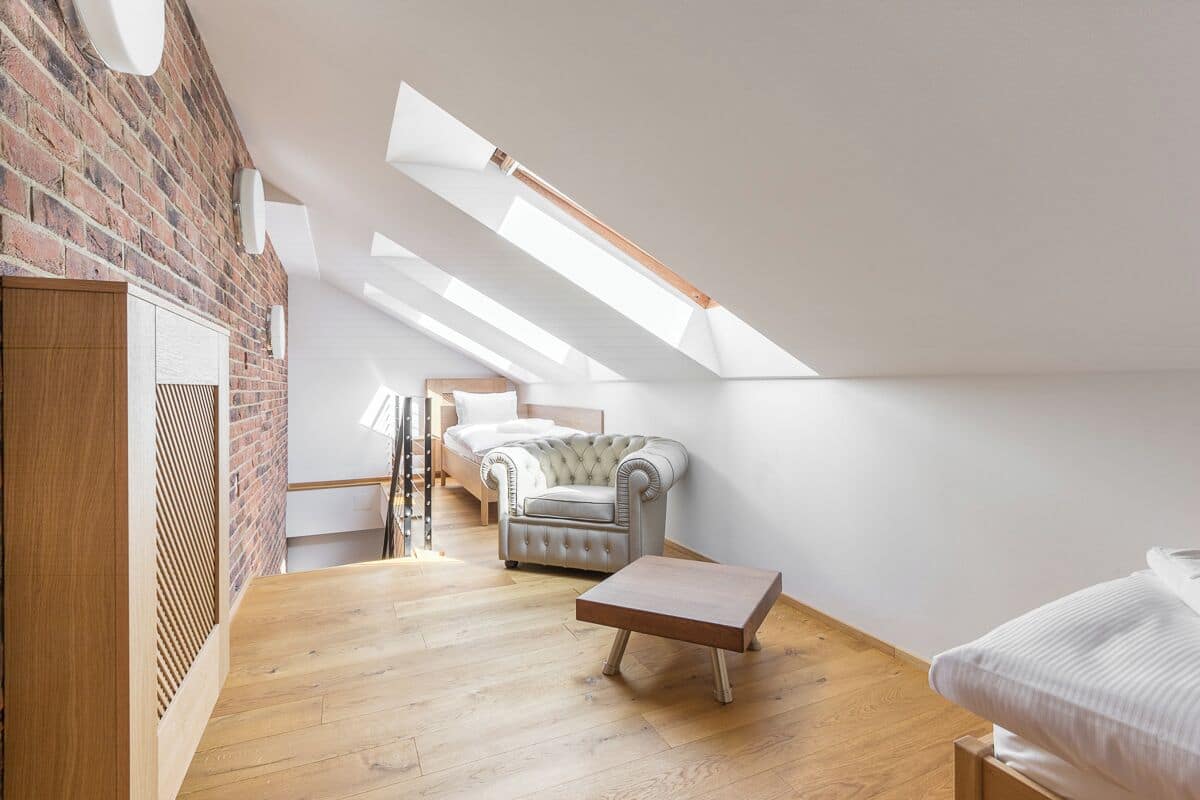 A loft bedroom with a sloped ceiling, a bed, a chaise lounge, and a wooden floor.