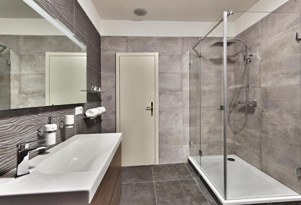 A modern bathroom with a glass shower enclosure, a white sink with a chrome faucet, and a large mirror.