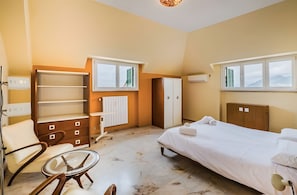 Quarto de hotel com cama, poltrona, mesinha, guarda-roupa e janela com vista para montanhas.