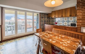 Un balcone con vista su edifici e montagne, un tavolo di legno con sedie, e una cucina con piastrelle decorate e mobili in legno.