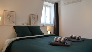 A bedroom with a bed, two pillows, a window with curtains, an air conditioner, and two framed artworks on the wall. - Le Cocon St Martin – Cozy Duplex in Nevers City Center, Air Conditioning (Nevers)