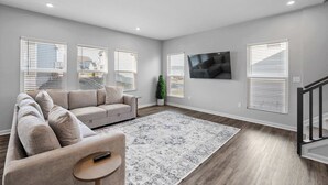 Un salon moderne avec un canapé d’angle beige, une petite table ronde et un tapis à motifs.