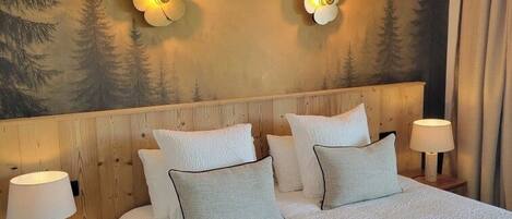 Una cama grande con ropa de cama blanca, dos lámparas de noche y un mural en la pared con una escena de bosque.