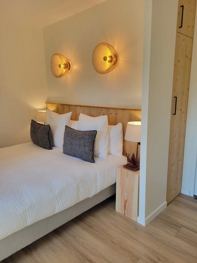 A bedroom with a bed, pillows, a nightstand, a lamp, and wall-mounted lights.