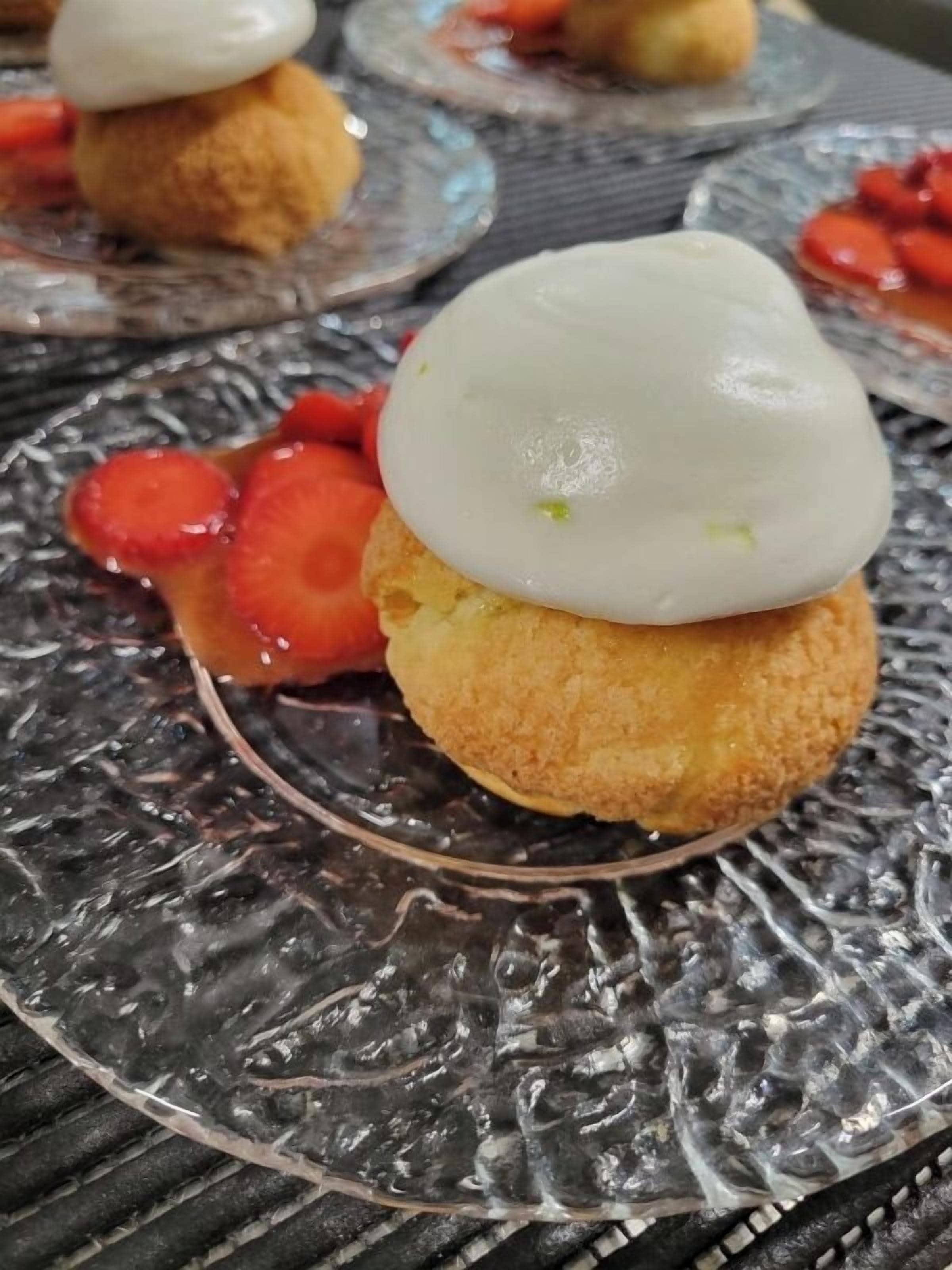 Un postre con cobertura blanca y fresas sobre un plato de vidrio texturizado.