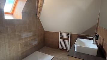 A bathroom with a shower, a sink, a window, and a radiator.