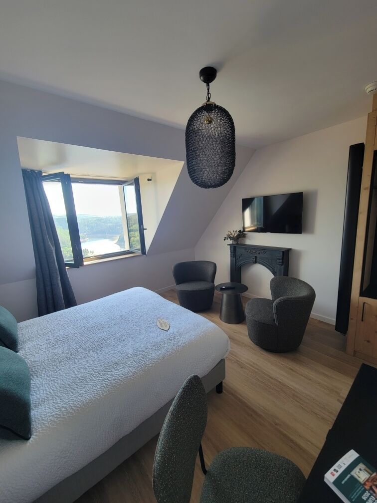 A modern room with a bed, two chairs, a small table, a TV, and a fireplace.