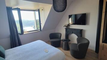 A modern room with a bed, two chairs, a small table, a TV, and a fireplace.